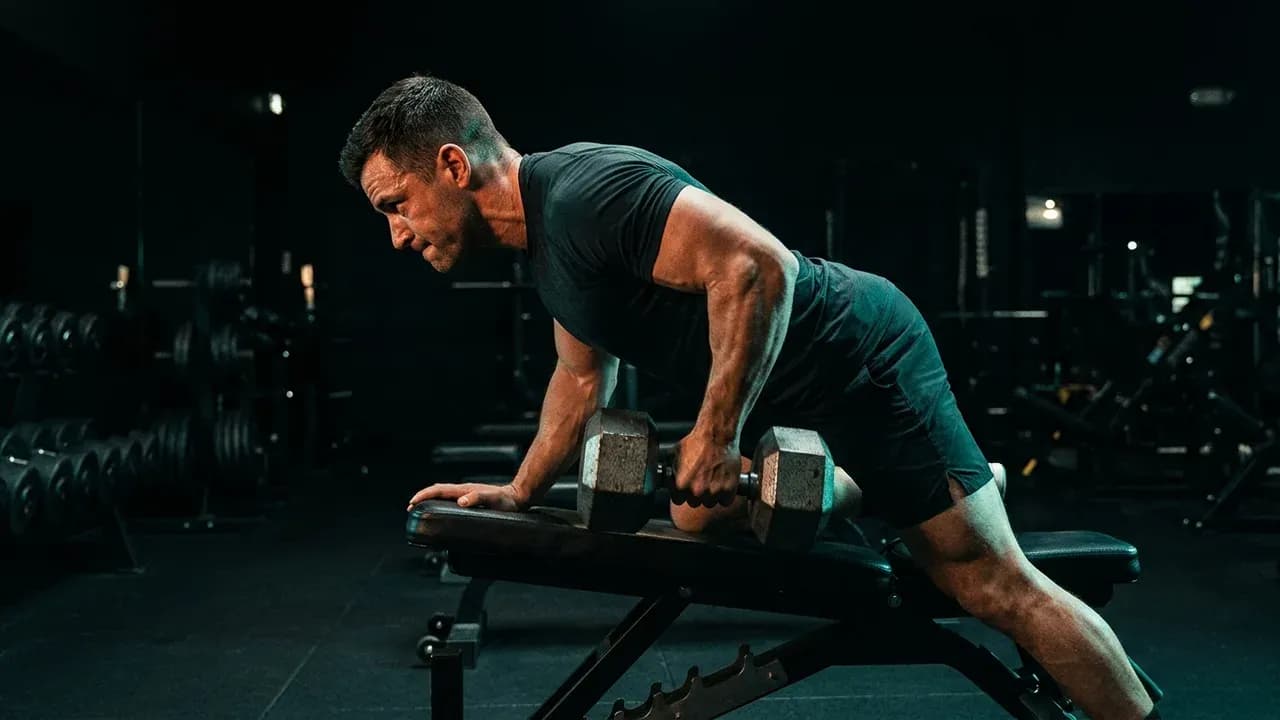 an athlete performing a heavy dumbbell row on an incline bench in a dark high-end strength conditioning gym